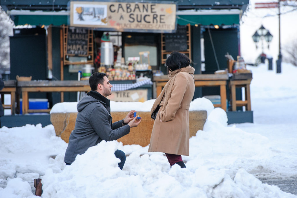 Man kneeling in the snow to propose to his girlfriend