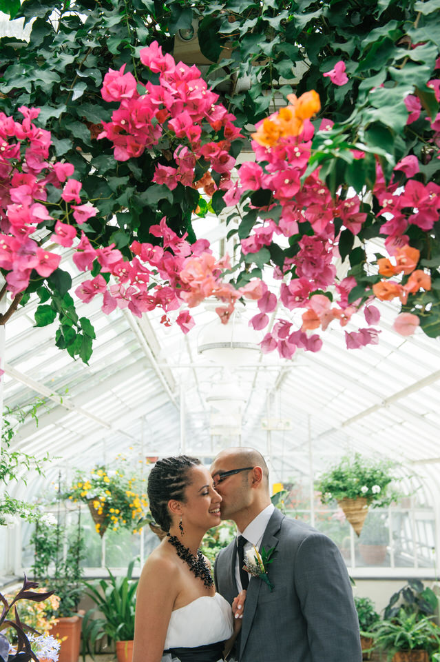 Marié embrassant la joue de sa femme en dessous d'une magnifique suspension florale dans la serre Westmount