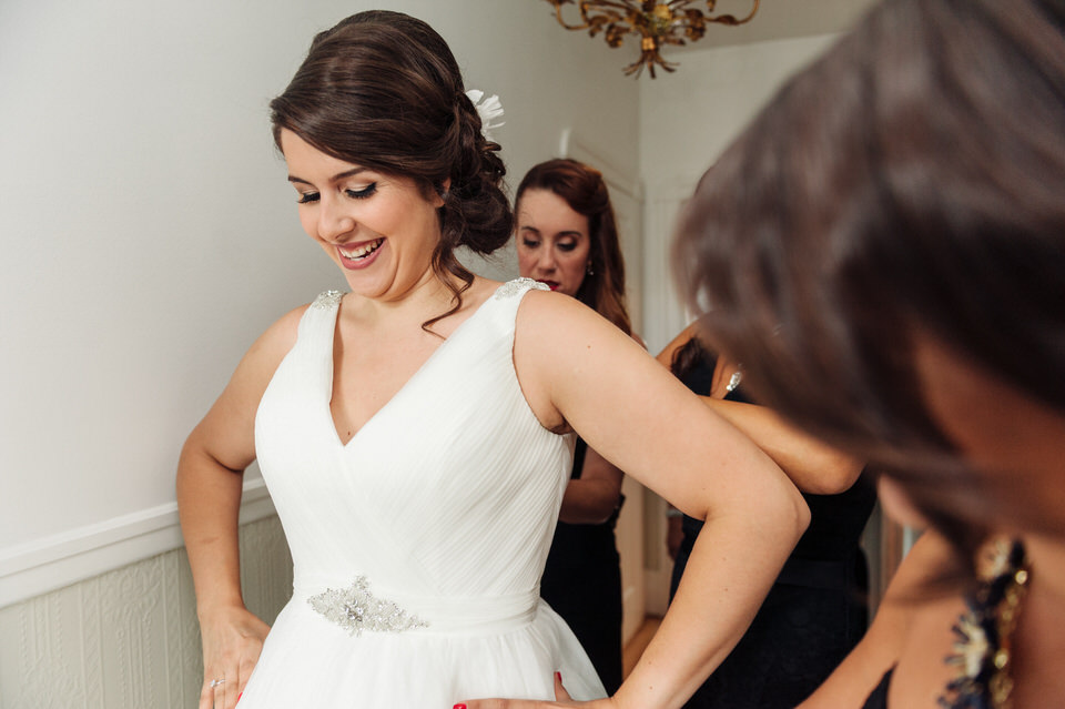 Friends buttoning up the bride's dress