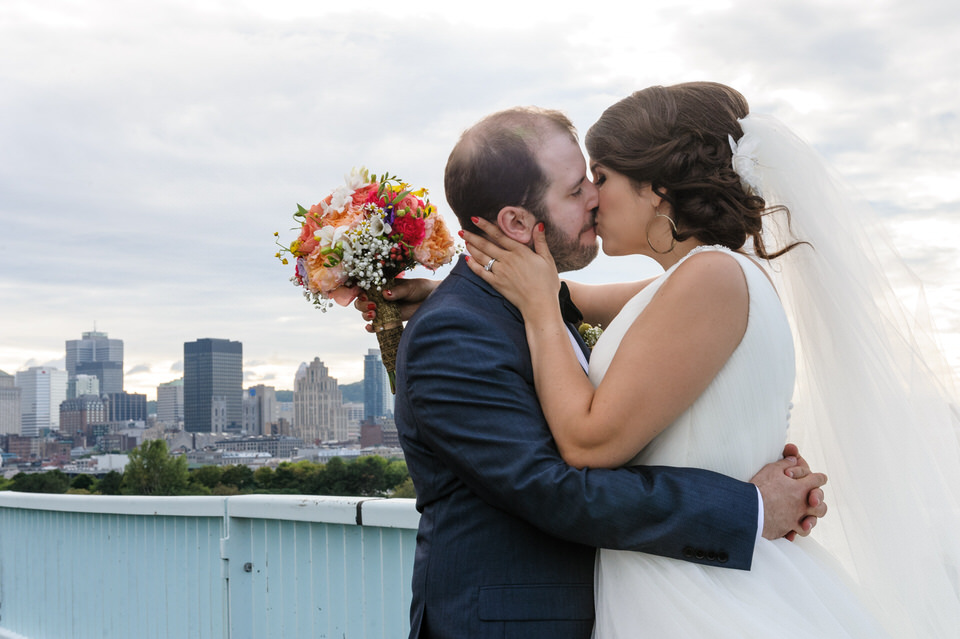 Bride and groom kissing on a bridge with view of Montreal behind them