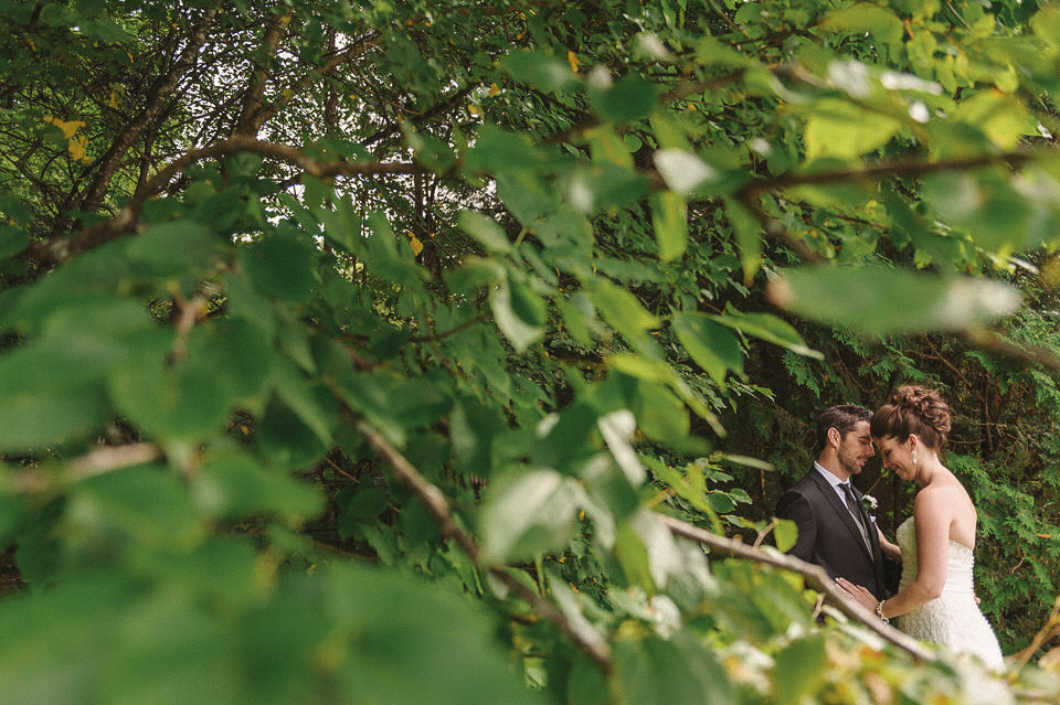 Moment intime entre les nouveaux mariés capturé à travers les branches vertes des arbres à Magog