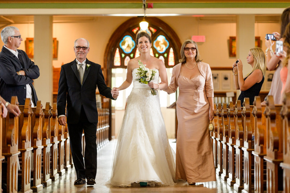 La mariée avance en direction de l'autel entourée par ses parents