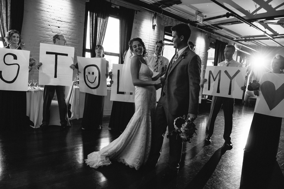 Wedding couple enters the reception while their wedding party holds signs