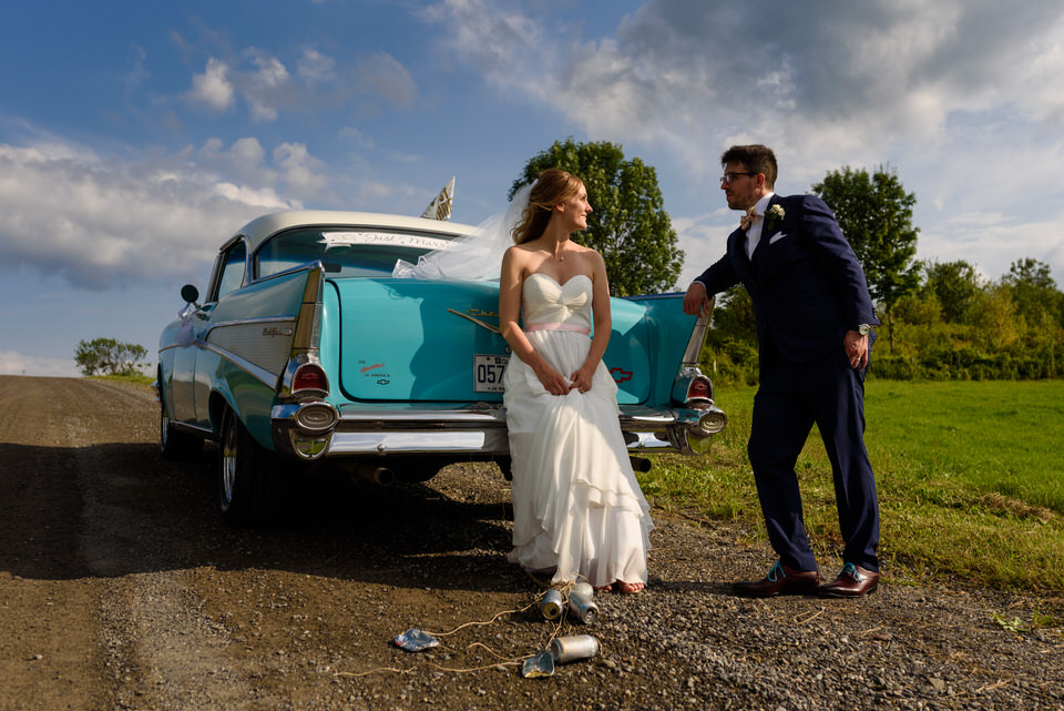 Portrait of bride and groom leaning on the back of a turquoise vintage car