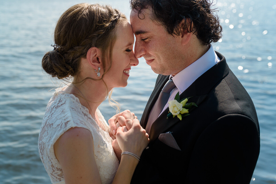 Wedding portrait of couple leaning close together at a lake