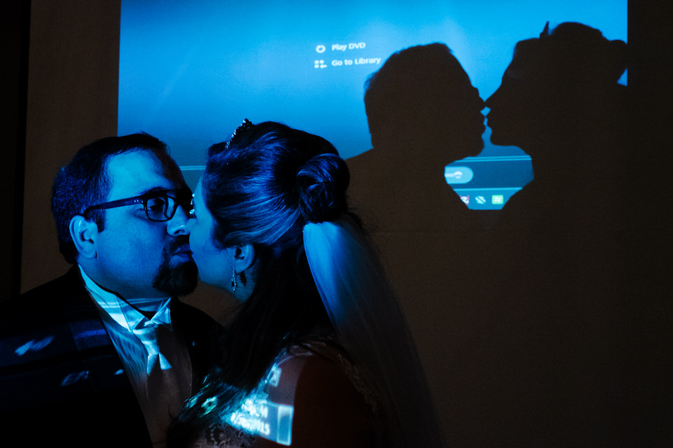 Bride and groom kissing in a dark room with a Powerpoint projector behind them