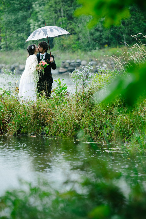 Mariés sous un parapluie a coté d'un lac sous la pluie