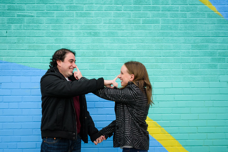 Engaged couple teasing each other in front of graffiti mural