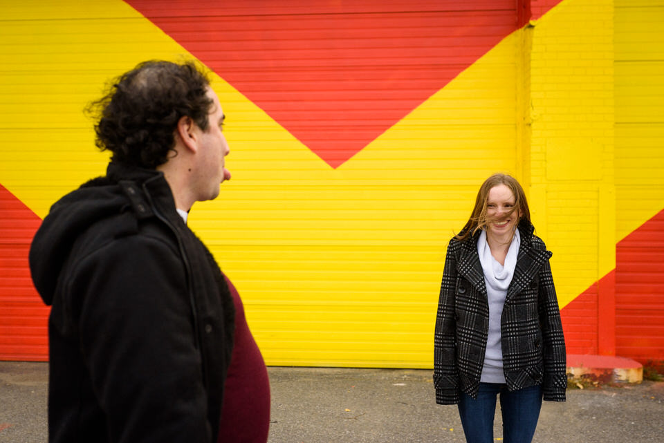 Guy making silly face to fiancée in front of graffiti mural in Montreal