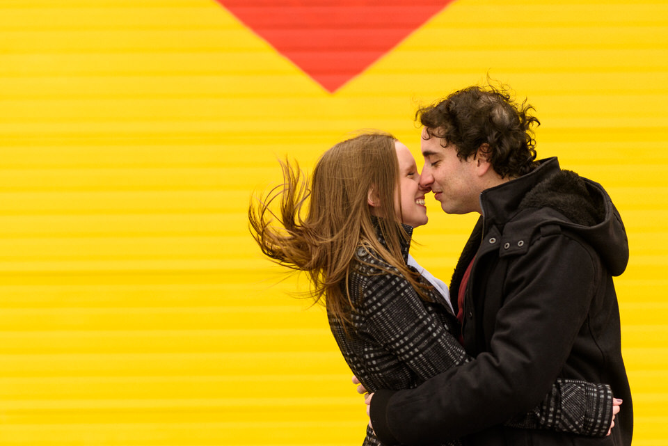 Newly engaged kissing in the wind in front of graffiti mural in Montreal
