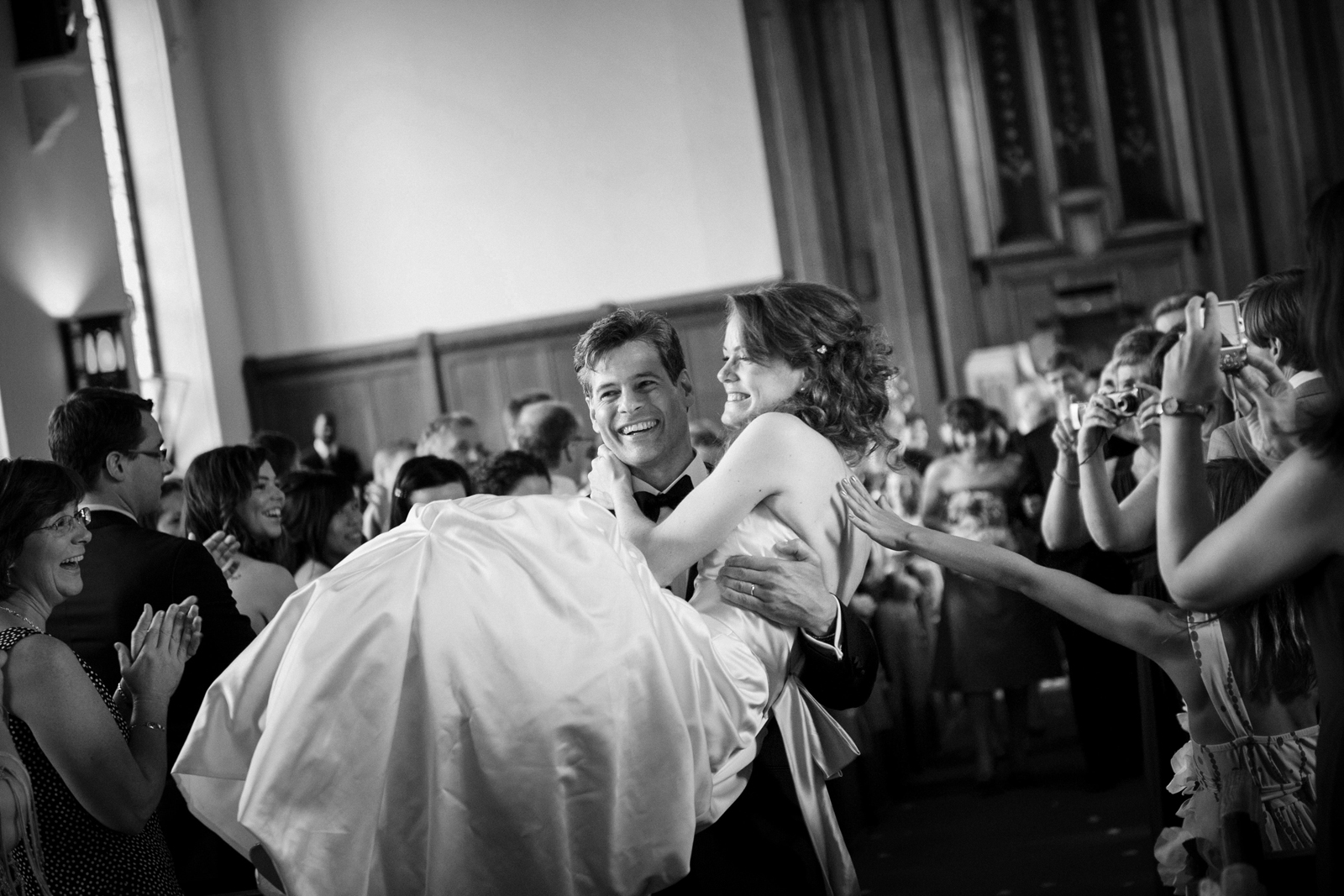 Groom carrying bride down aisle and a guest's hand reaches out to touch her from the crowd