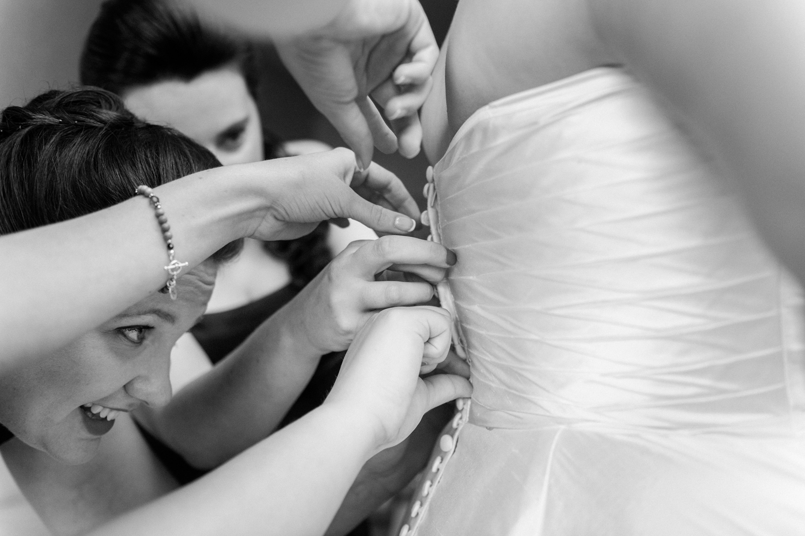 Bridesmaids working together to buttoning up wedding dress