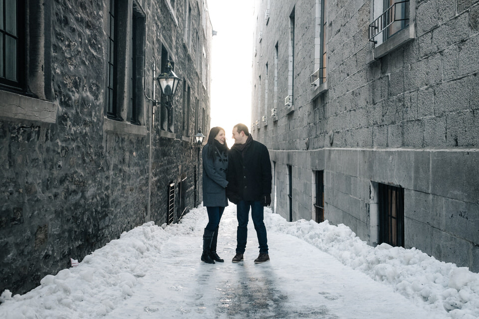 Engaged couple holding hands and looking at each other in snowy old Montreal streets