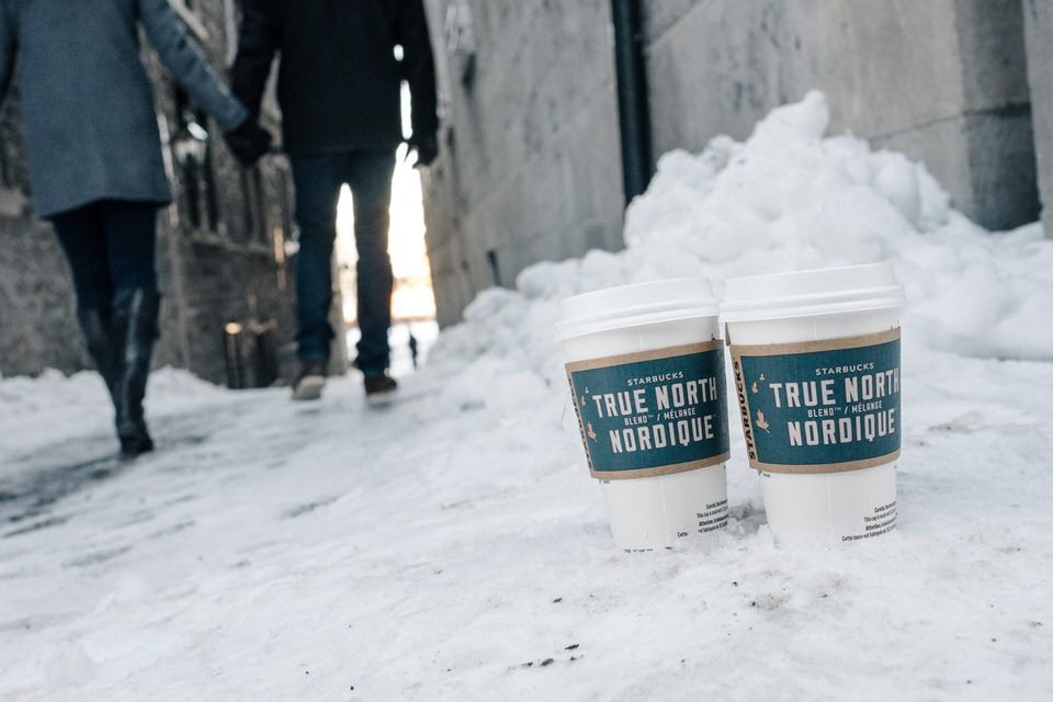 Close up of two cup of coffee in the snow as a couple walks away