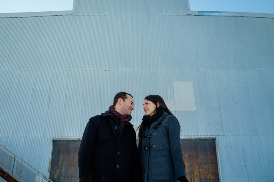 couple smiling at each other in front of an old empty warehouse door