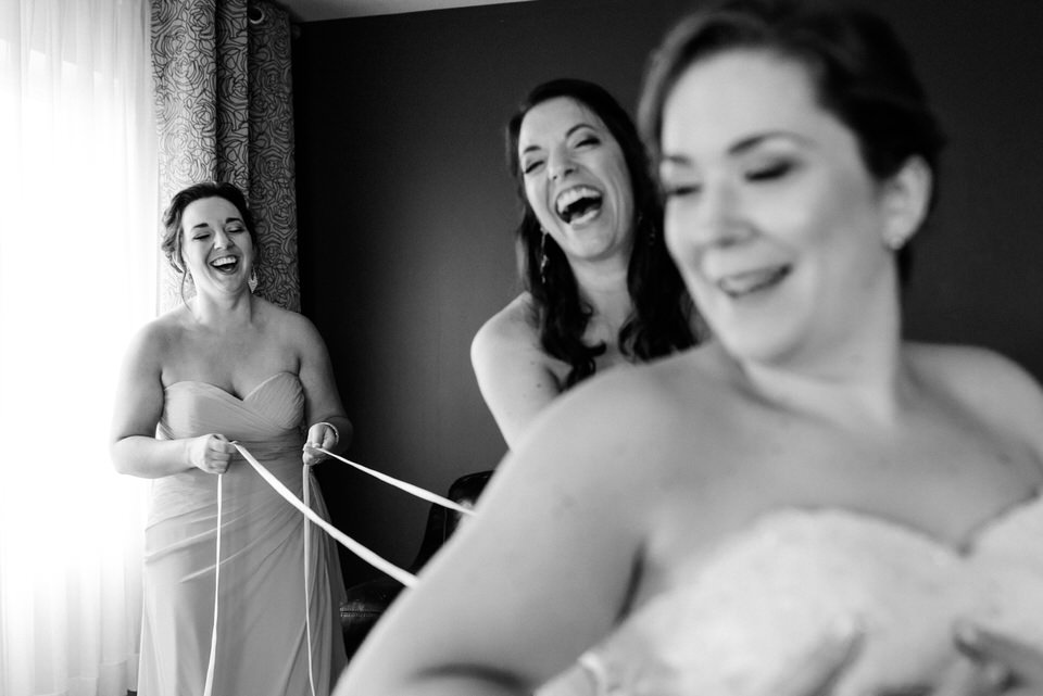 Candid photo of bridesmaids lacing up the bride's dress