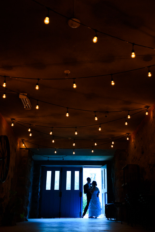Silhouette of bride and groom dancing old coach house sheltered from rain