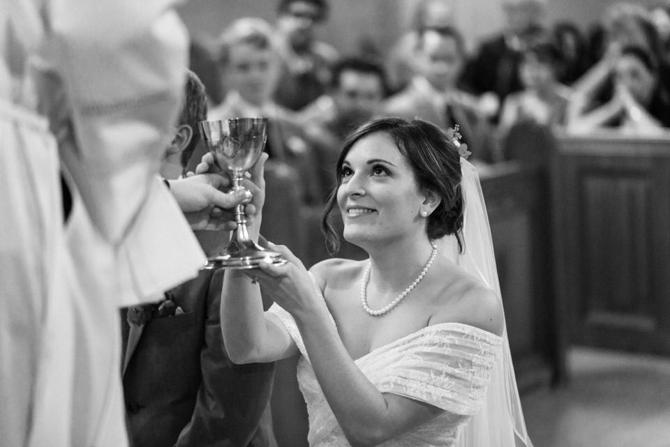 Bride kneeling in front of priest taking communion 