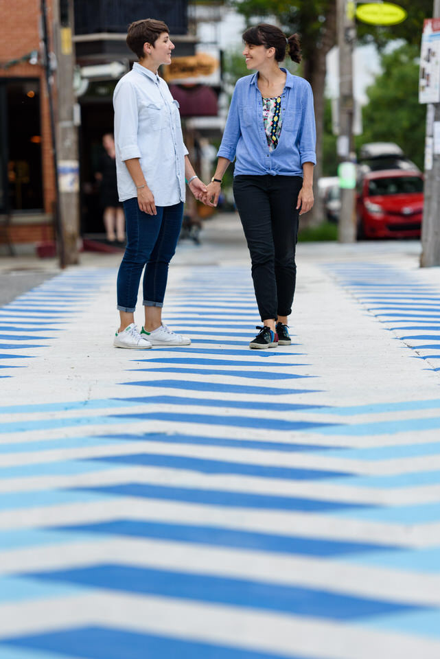 Lesbian couple holding hands on colourful sidewalk in Montreal