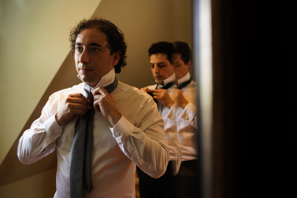 Groom tying tie in mirror