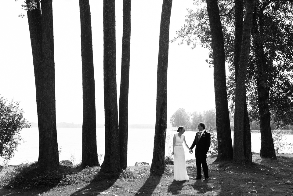 Bride and groom standing on the riverside in a row of tall trees