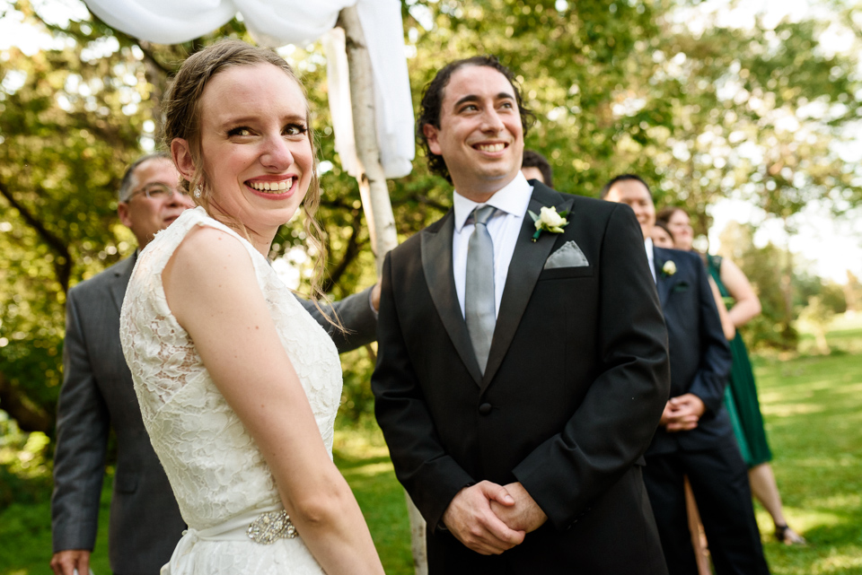Bride and groom smiling at their guests during wedding ceremony outdoors