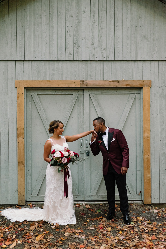 Groom kissing bride's hand in front of rustic barn door at Chalet des Erables