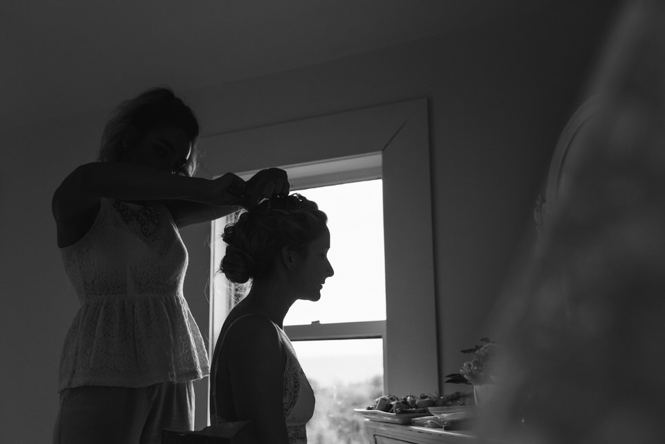 Bride silhouetted against window as she gets her wedding hair done