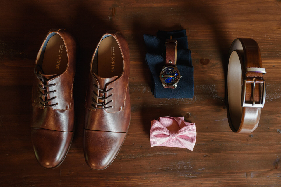 Flat lay photo of groom's accessories on wooden floor (shoes, bowtie, watch, socks and belt)