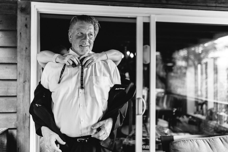 Hands reaching around man's neck as he gets a bow tie on