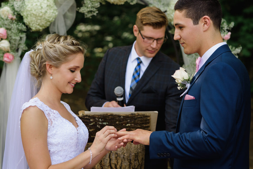 Bride putting ring on groom at rustic wedding