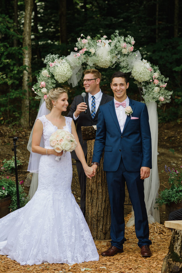 Bride and groom holding hands in front of floral archway at outdoor wedding