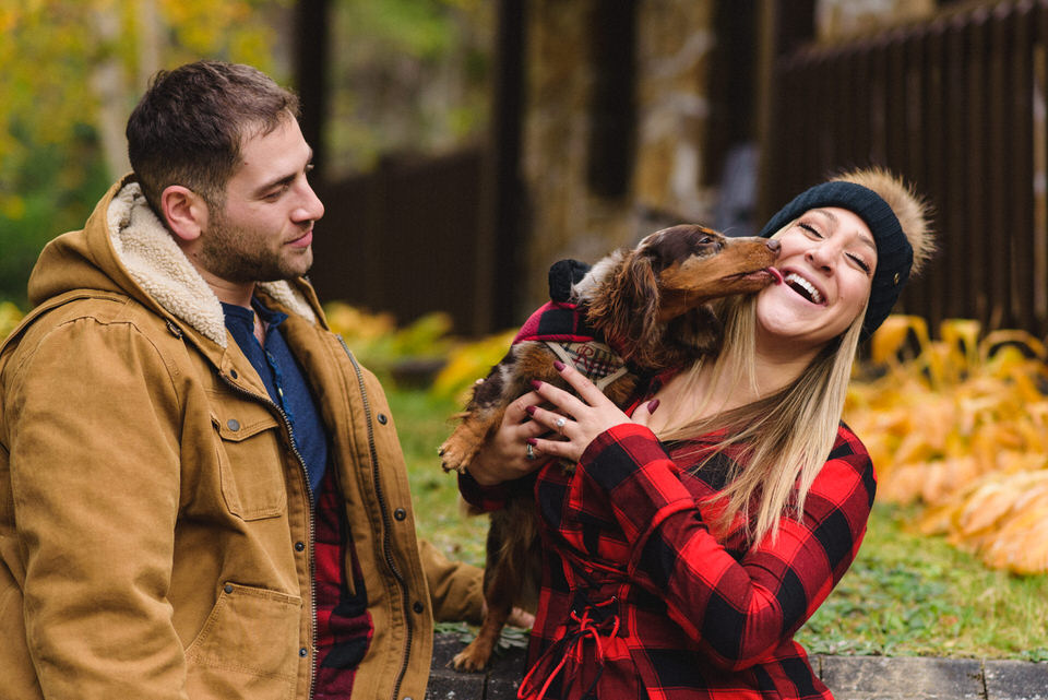 Engagement photo with dog licking woman's face as her fiancé looks on