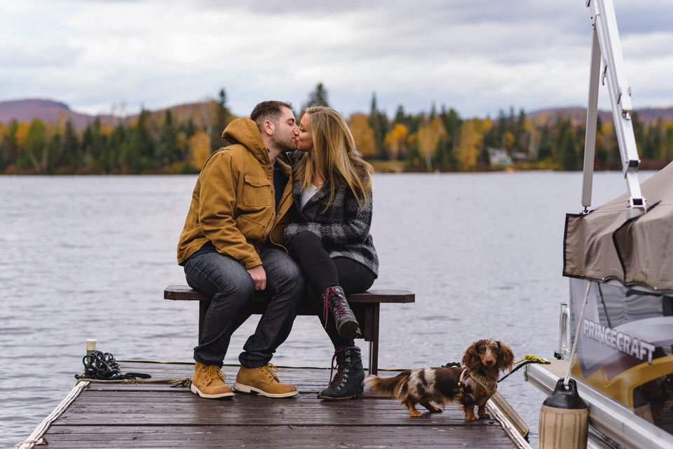 Couple kissing on dock with dachshund at their feet