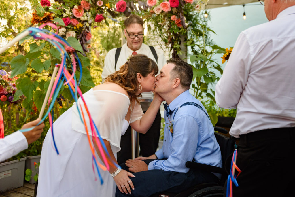 Bride and groom kissing at ceremony as guests wave streamers