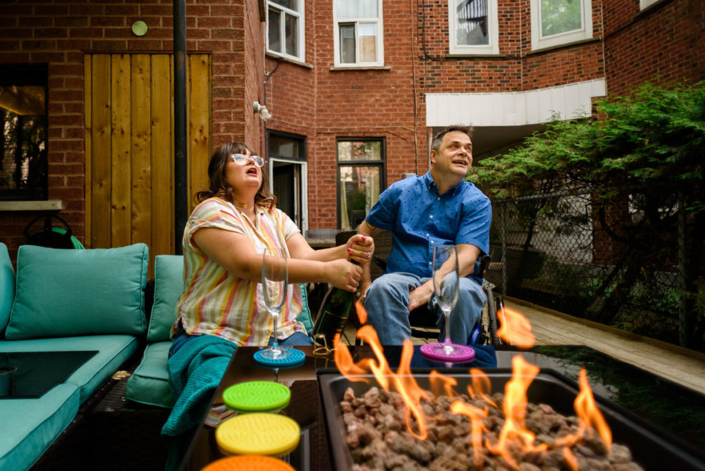 Woman popping champagne in front of a fire pit in backyard