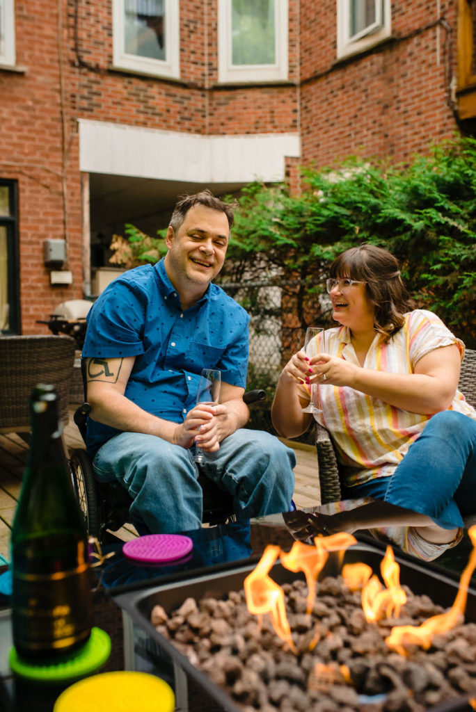 Engagement photo of couple popping champagne in front of a fire pit in backyard