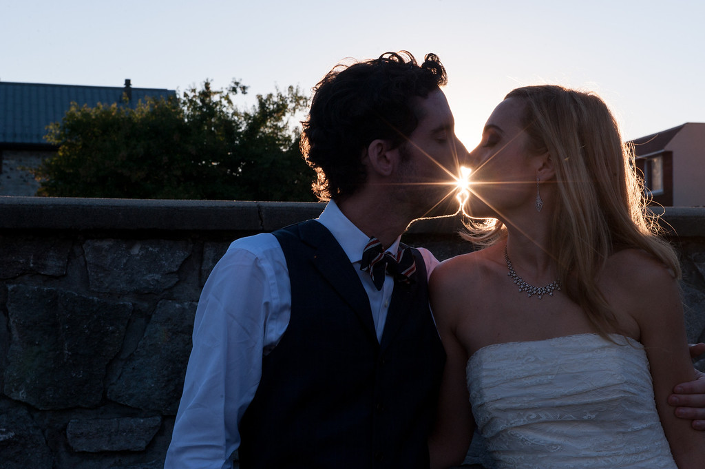 Silhouette of bride and groom kissing at sunset with sun flare