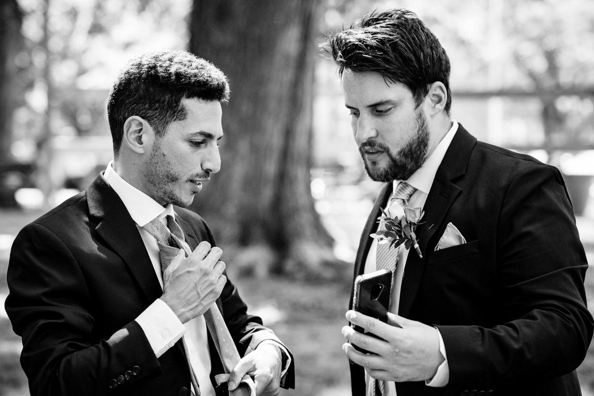 Friend holding phone so the groom can tie his tie