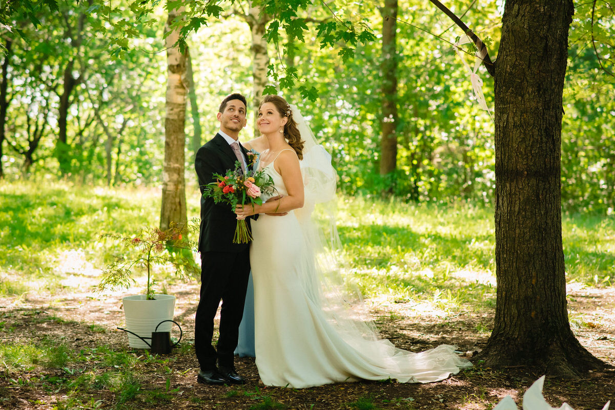 Bride and groom look around at trees in park wedding