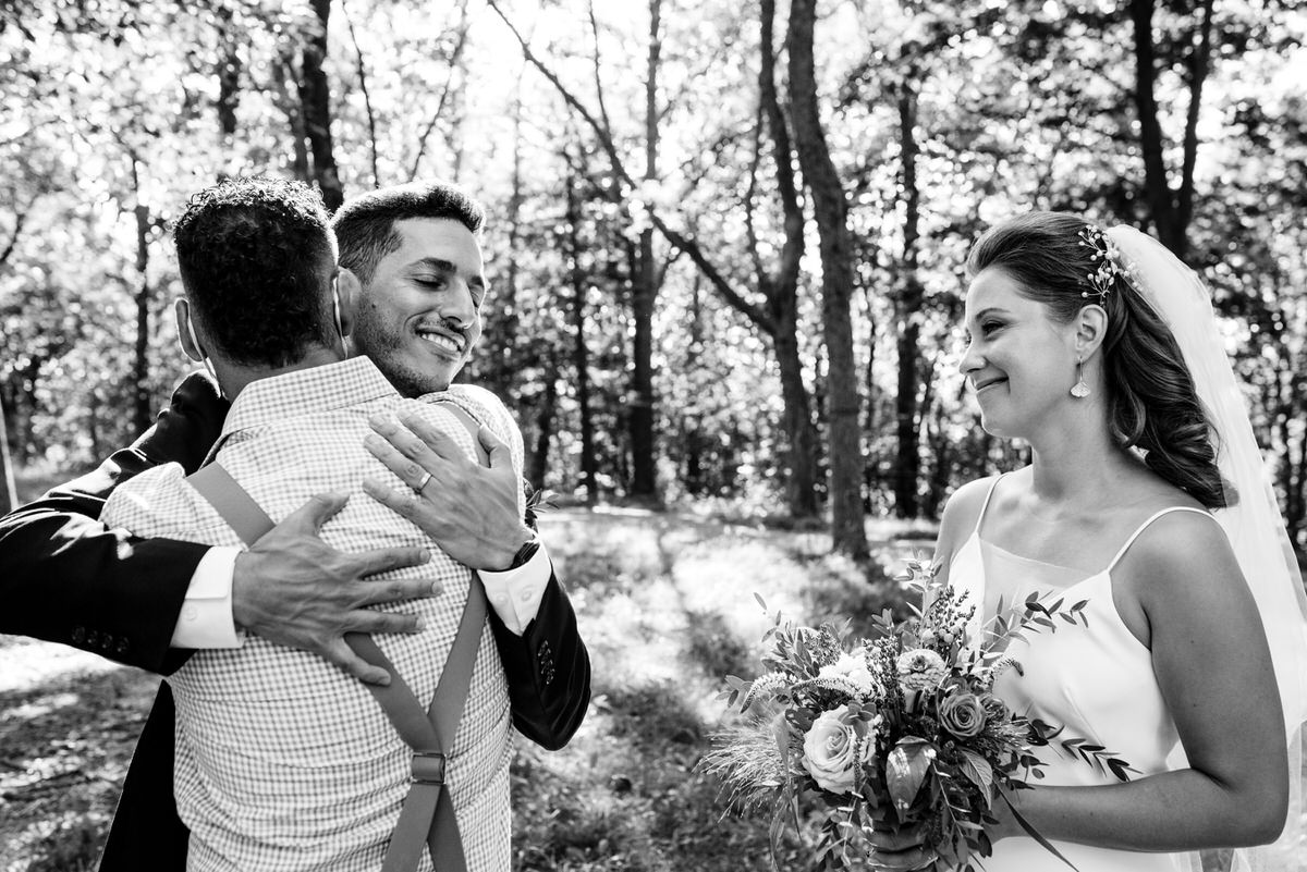 Groom receives a hug from family member as bride looks on