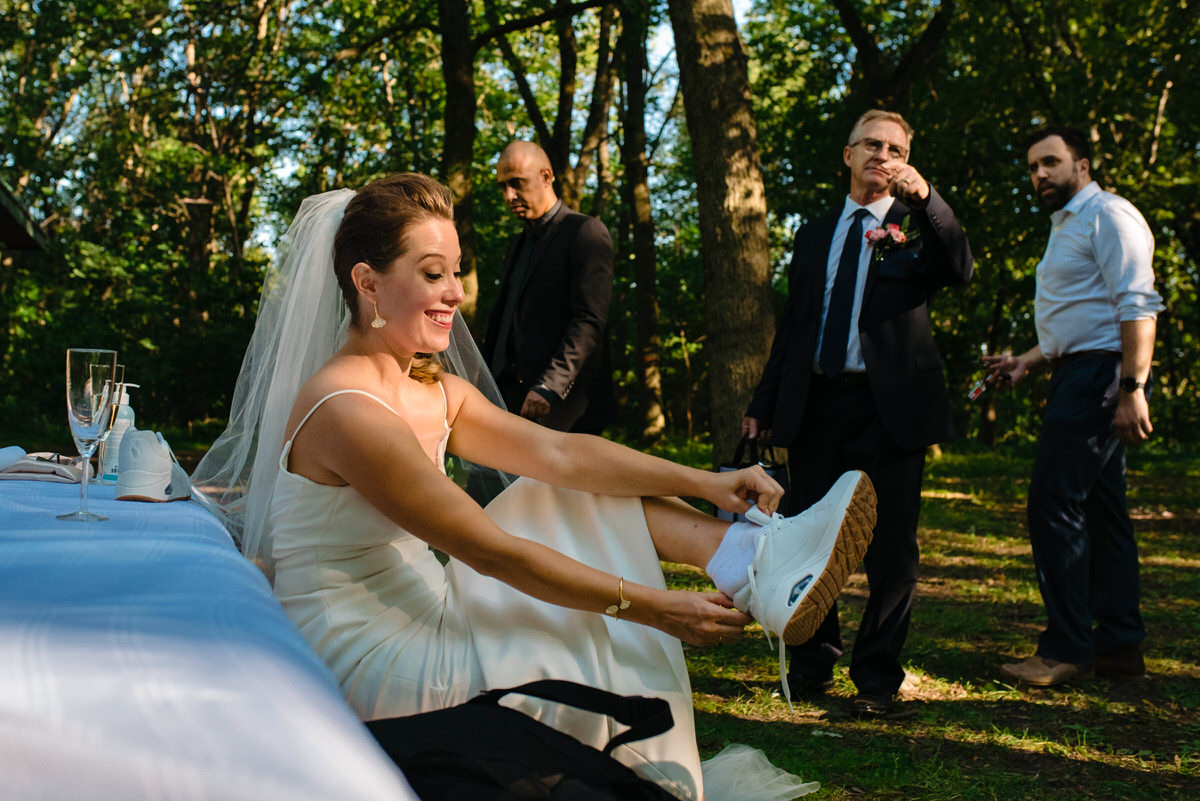 Bride putting on running shoes for her wedding photos in the park