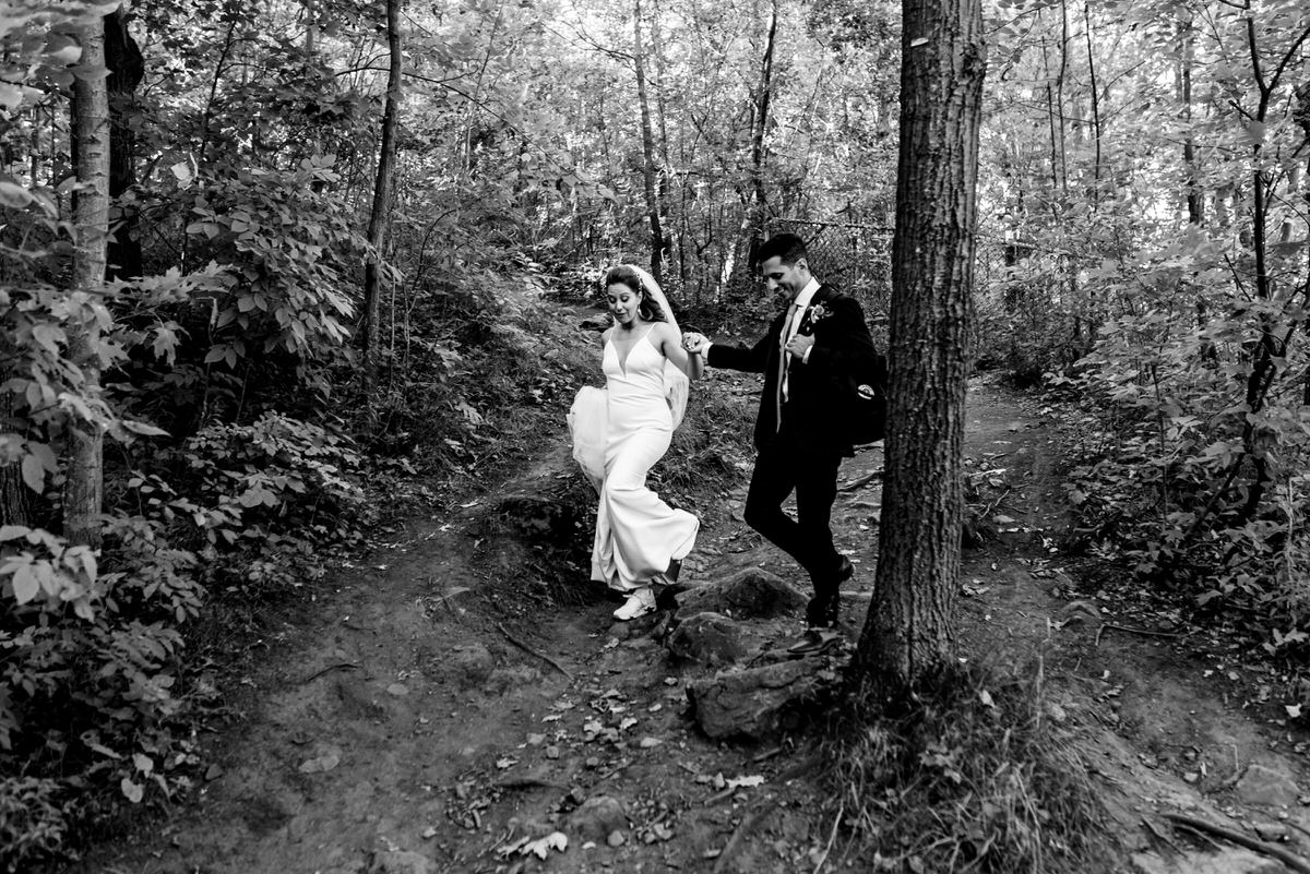 Groom leading bride down a rocky path through the woods