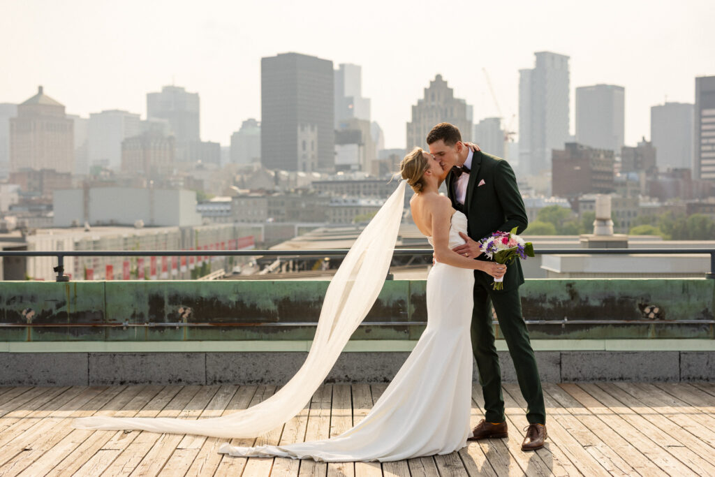 Bride and groom kissing on the rooftop of the Montreal Science Centre with a panoramic skyline behind them