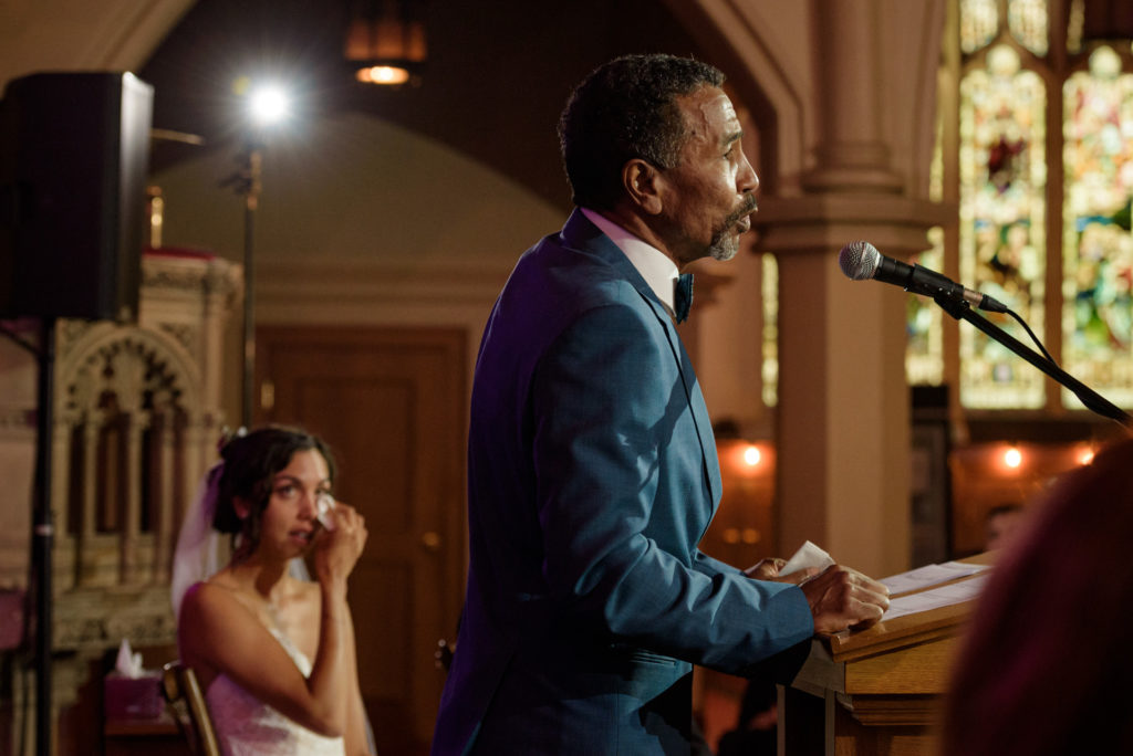 Father of the bride speaking at wedding ceremony as bride wipes her eyes