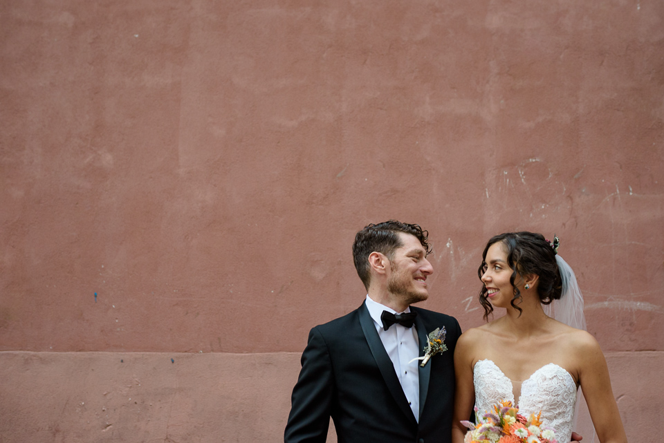 Wedding couple looking at each other in front of pink concrete wall