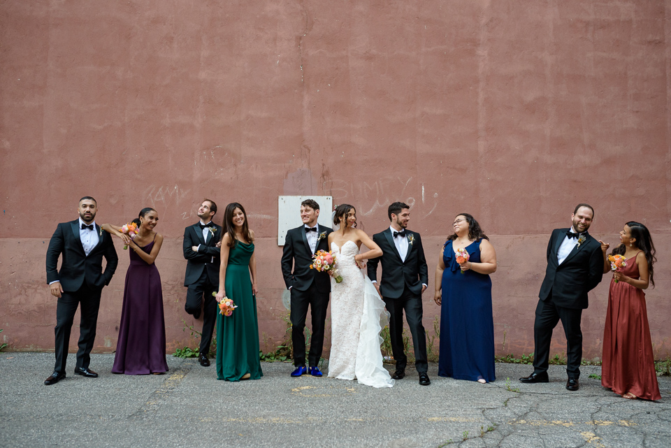 Wedding party having fun with silly poses in from of pink concrete wall