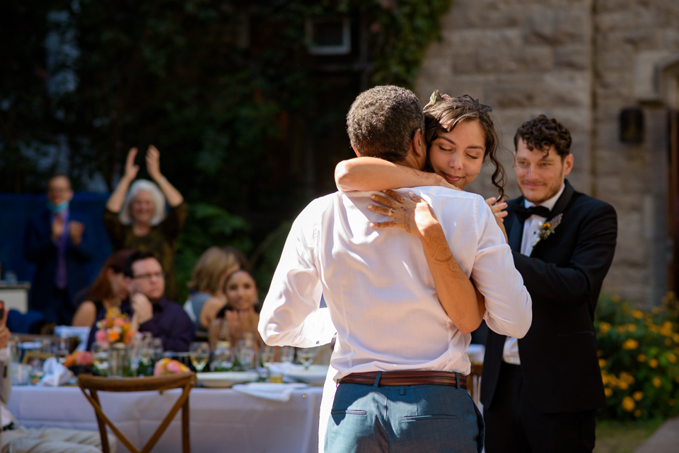 Bride hugging her father as aunt claps in the background