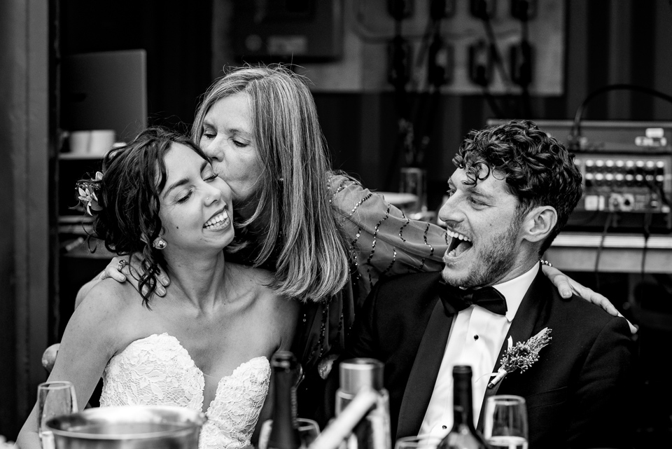 Mom kissing the bride's cheek as groom grins