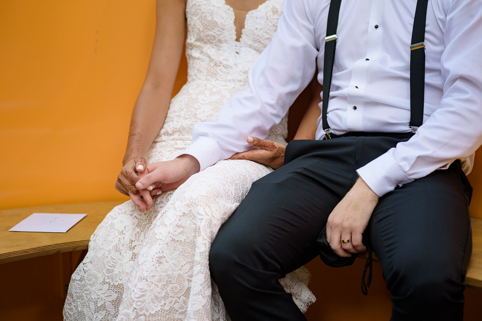 Close up of wedding couple holding hands as they sit on a yellow bench